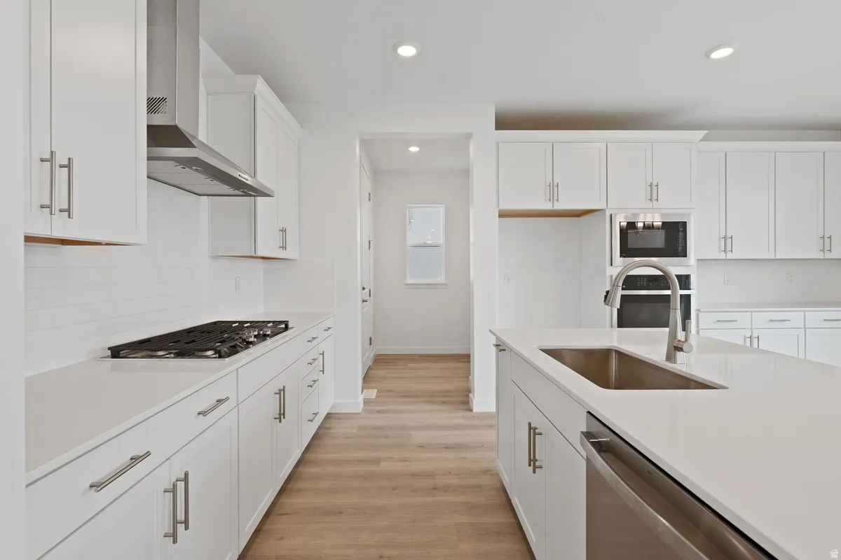 Kitchen with backsplash, white cabinets, wall chimney exhaust hood, stainless steel appliances, and recessed lighting