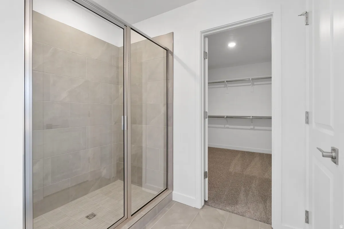 Full bathroom with light colored carpet, a shower stall, a walk in closet, light tile patterned floors, and recessed lighting