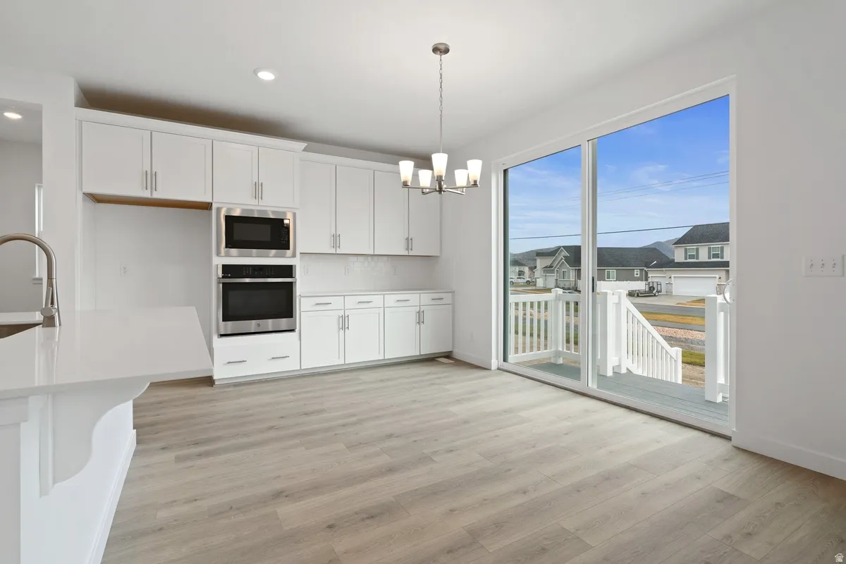 Kitchen featuring white cabinetry, appliances with stainless steel finishes, light wood-type flooring, pendant lighting, and backsplash