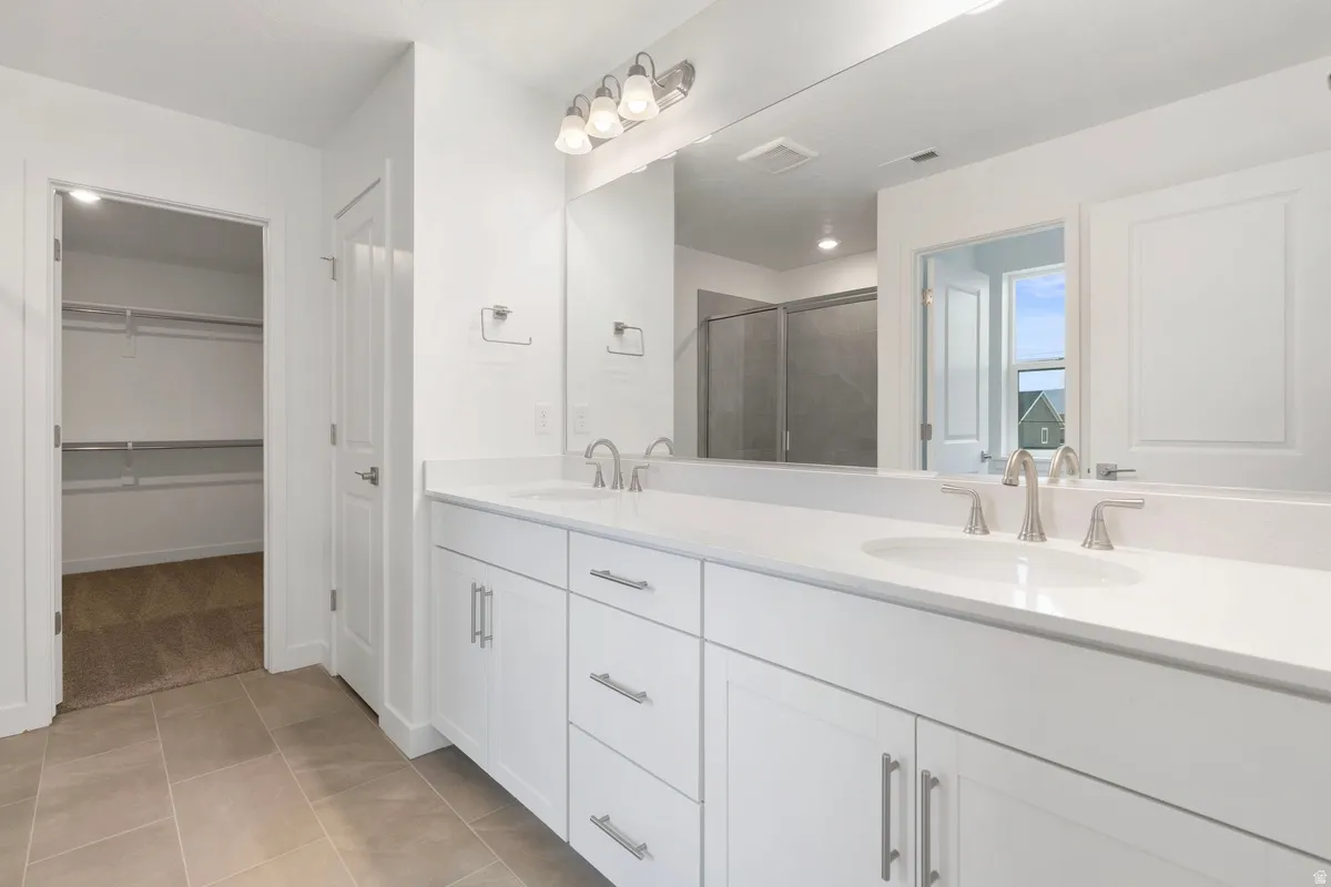 Full bath featuring a spacious closet, double vanity, a shower stall, light tile patterned floors, and light colored carpet