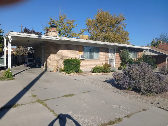 View of front of house featuring brick siding, concrete driveway, a chimney, and a carport