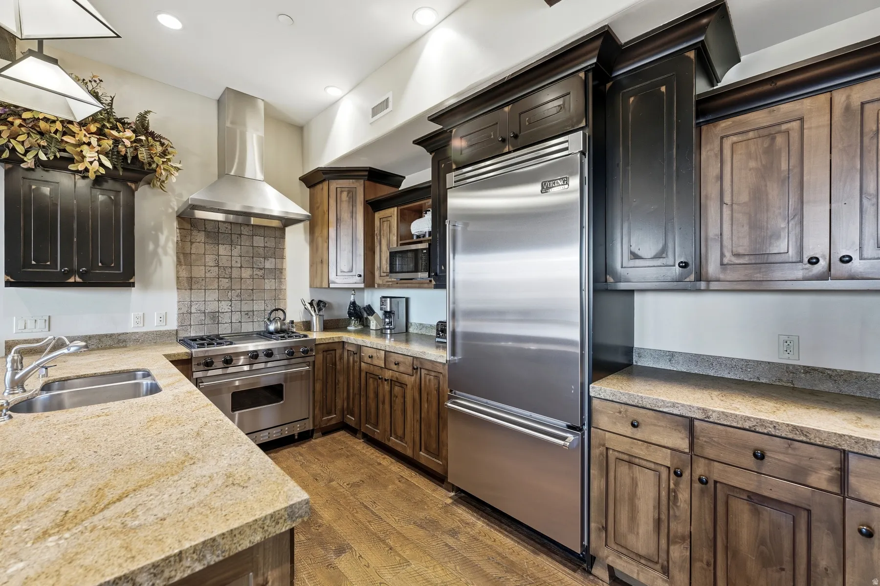 Kitchen featuring premium appliances, wall chimney exhaust hood, dark wood finished floors, light stone counters, and recessed lighting