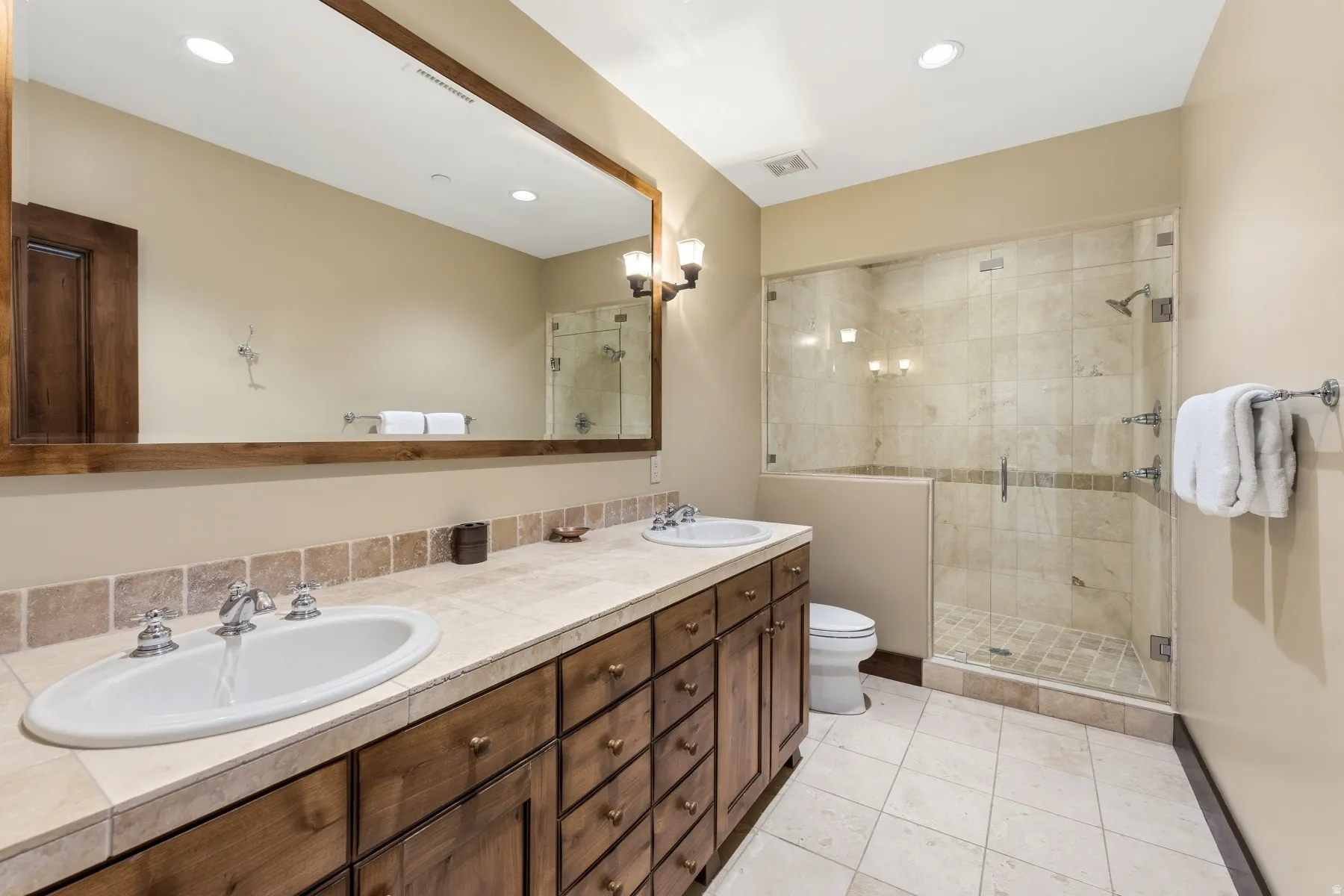 Full bath with double vanity, a shower stall, light tile patterned floors, and recessed lighting