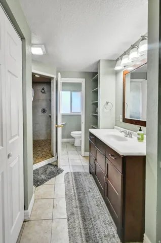 Bathroom with a textured ceiling, a shower stall, vanity, light tile patterned flooring, and a closet