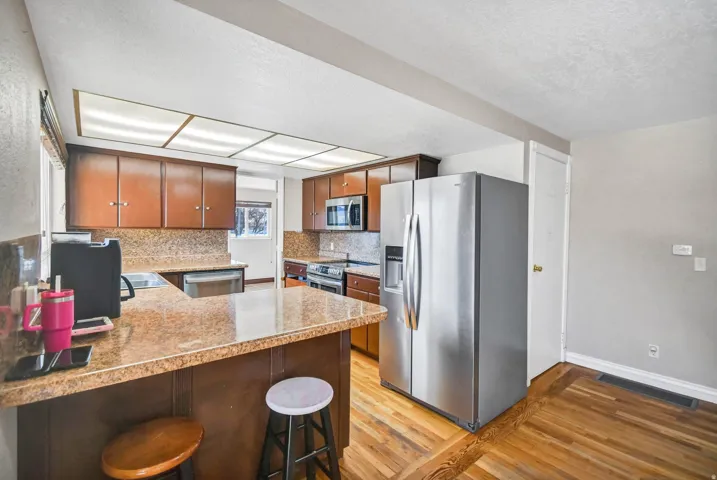 Kitchen featuring appliances with stainless steel finishes, a peninsula, light wood-type flooring, a kitchen breakfast bar, and backsplash
