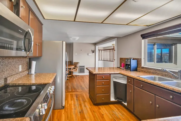 Kitchen with stainless steel appliances, a peninsula, tasteful backsplash, light wood-style flooring, and brown cabinets