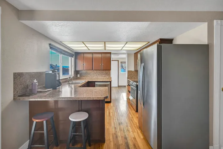 Kitchen with stainless steel appliances, brown cabinetry, light wood finished floors, decorative backsplash, and a peninsula