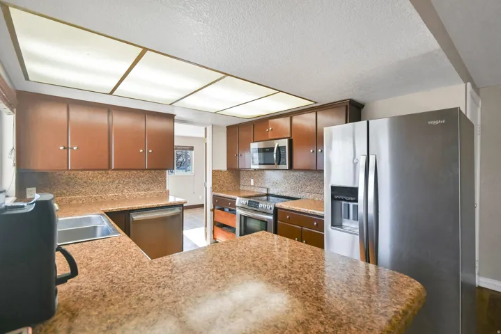 Kitchen featuring appliances with stainless steel finishes, tasteful backsplash, a textured ceiling, a peninsula, and light stone counters