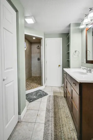 Full bathroom featuring light tile patterned floors, a textured ceiling, a stall shower, and vanity