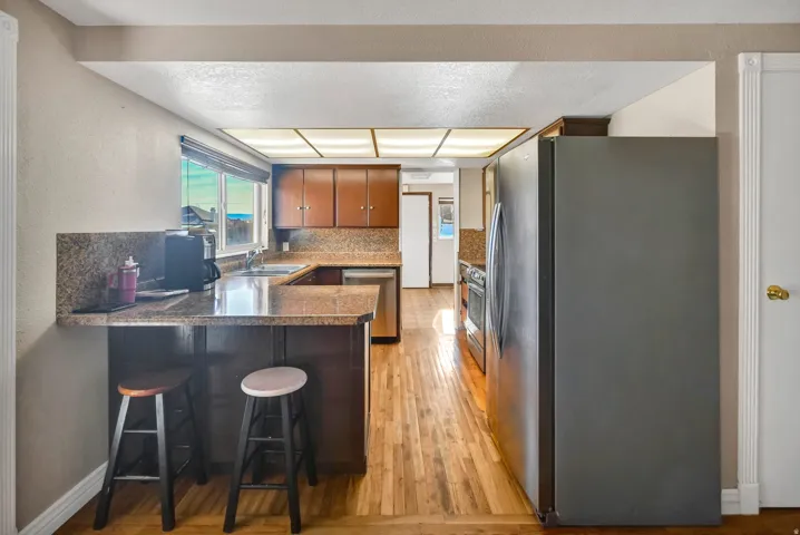 Kitchen featuring appliances with stainless steel finishes, a breakfast bar, a peninsula, light wood finished floors, and brown cabinetry