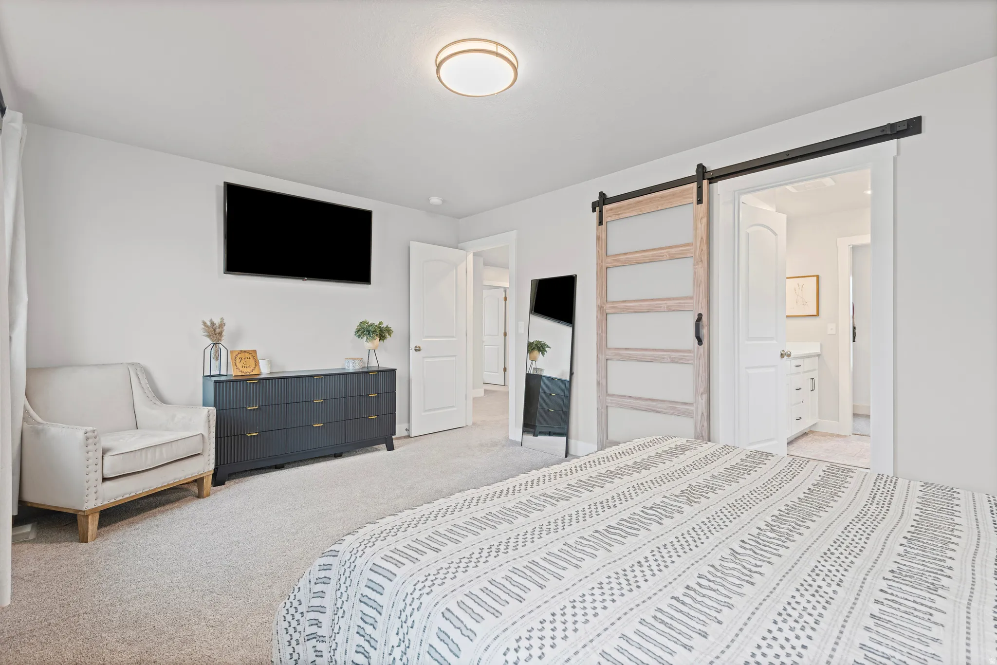 Primary bedroom with a barn door, light colored carpet, and connected primary bathroom