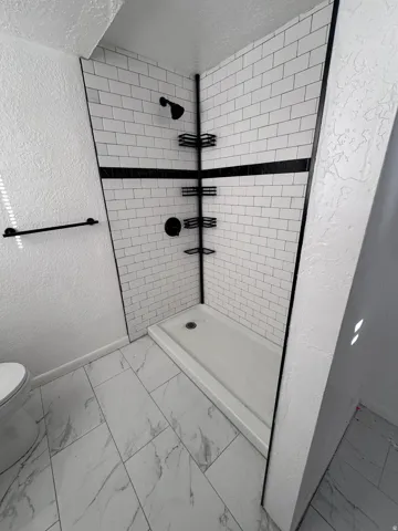 Bathroom featuring a textured wall, marble look tile flooring, a shower stall, and a textured ceiling