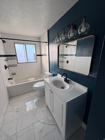 Full bath featuring washtub / shower combination, a textured ceiling, vanity, light marble finish floors, and a textured wall