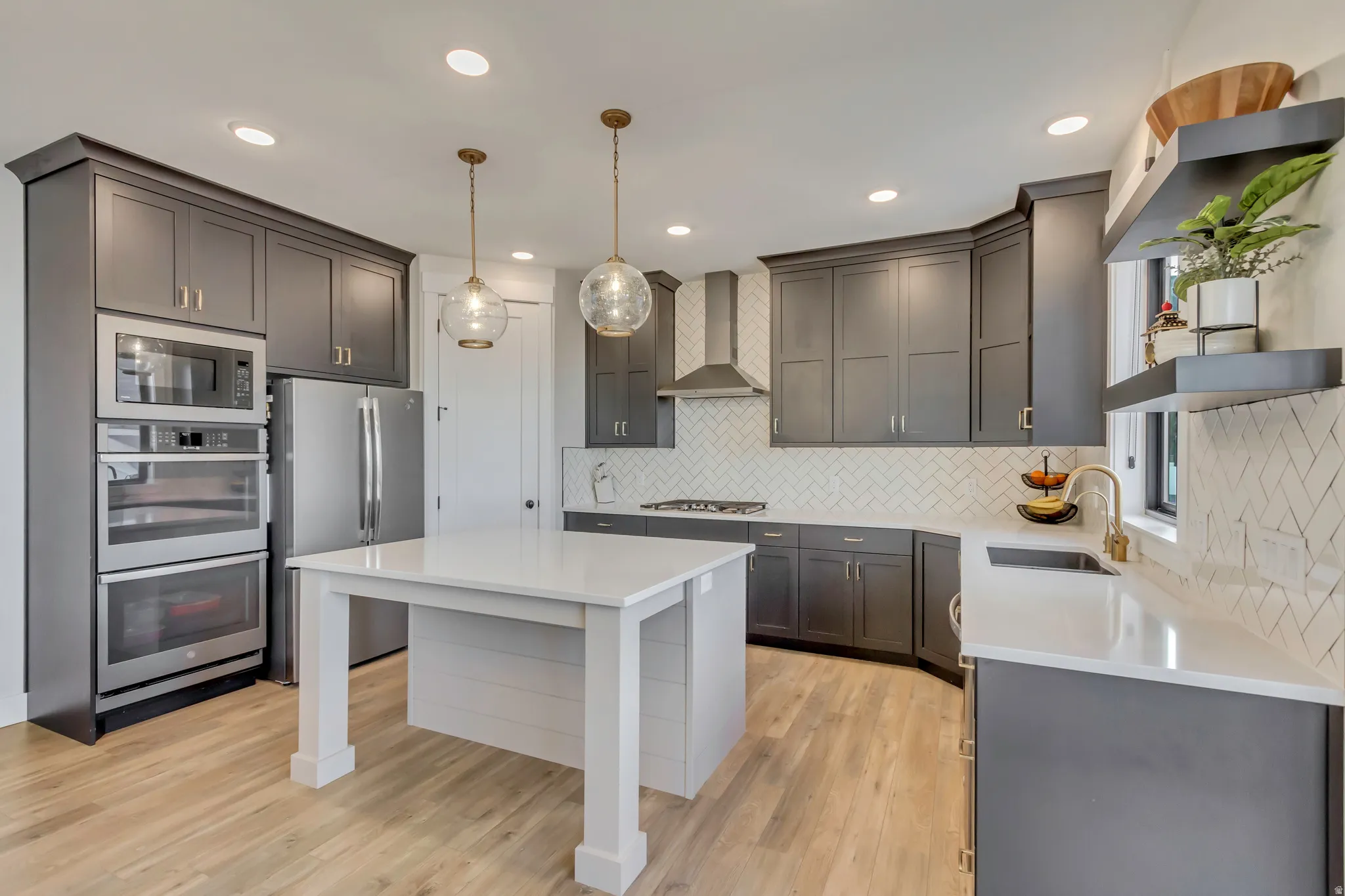 Kitchen featuring hanging light fixtures, stainless steel appliances, wall chimney exhaust hood, light stone countertops, and a center island