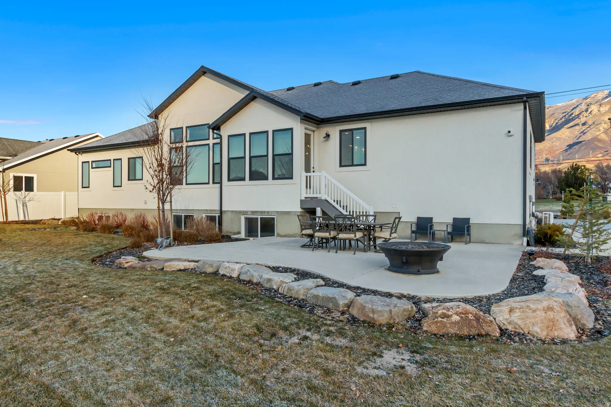 Rear view of property featuring a patio area, stucco siding, a fire pit, a lawn, and roof with shingles