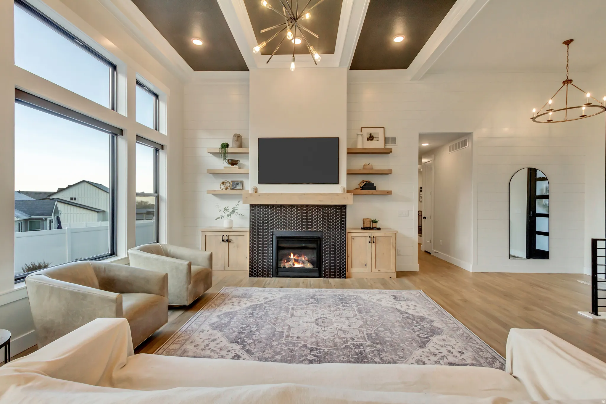 Living area with a chandelier, beam ceiling, light wood finished floors, a tiled fireplace, and a high ceiling