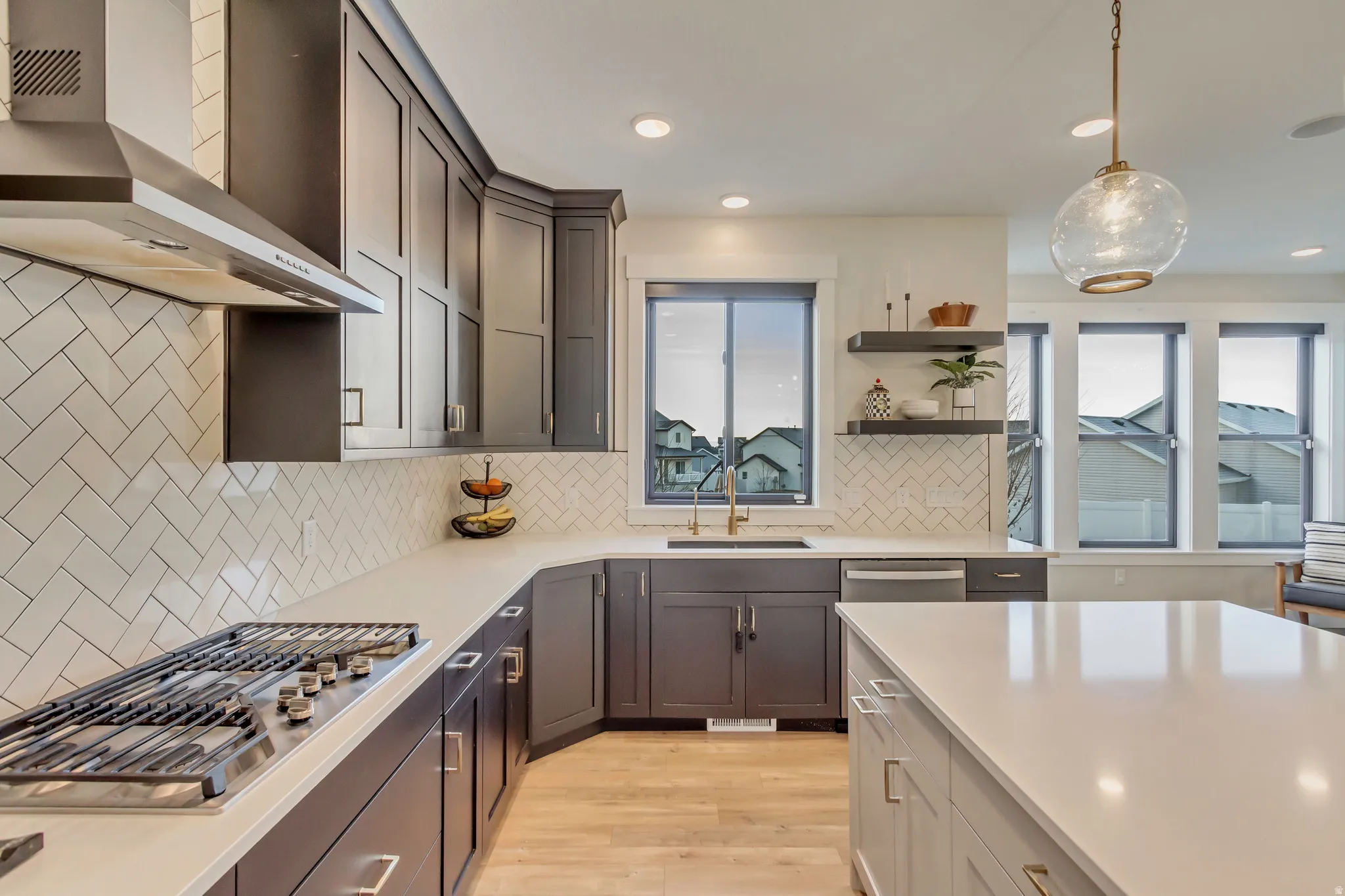 Kitchen featuring wall chimney range hood, decorative light fixtures, stainless steel appliances, light wood-style floors, and backsplash