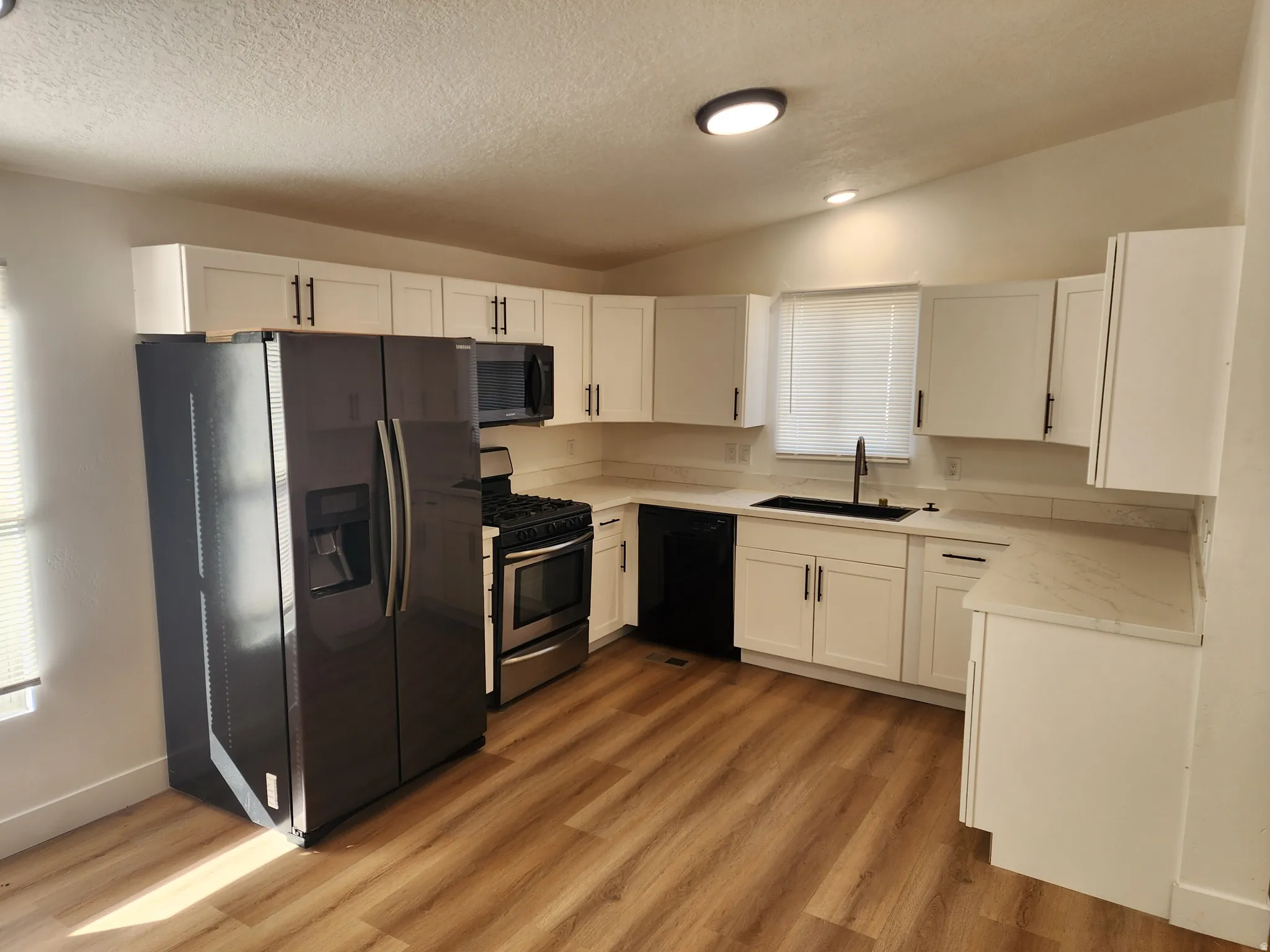 Kitchen with black appliances, white cabinets, lofted ceiling, light wood-type flooring, and a textured ceiling