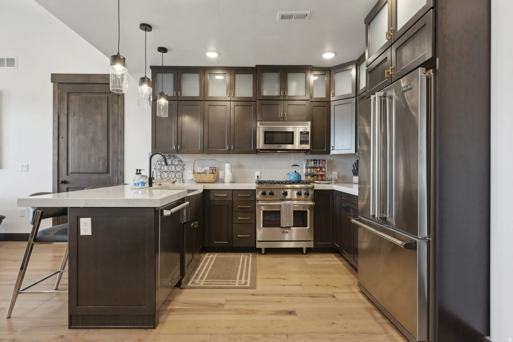 Kitchen featuring a peninsula, dark brown cabinetry, pendant lighting, high end appliances, and a kitchen breakfast bar