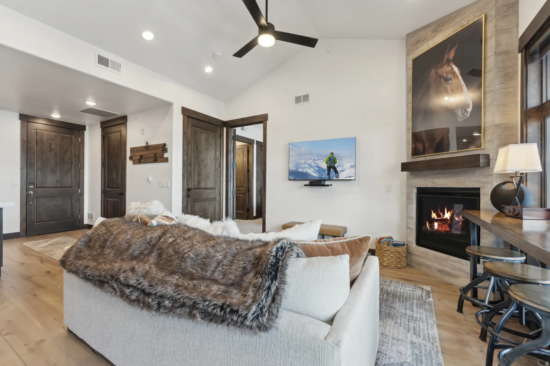 Living room with lofted ceiling, a tile fireplace, light wood-type flooring, a ceiling fan, and recessed lighting