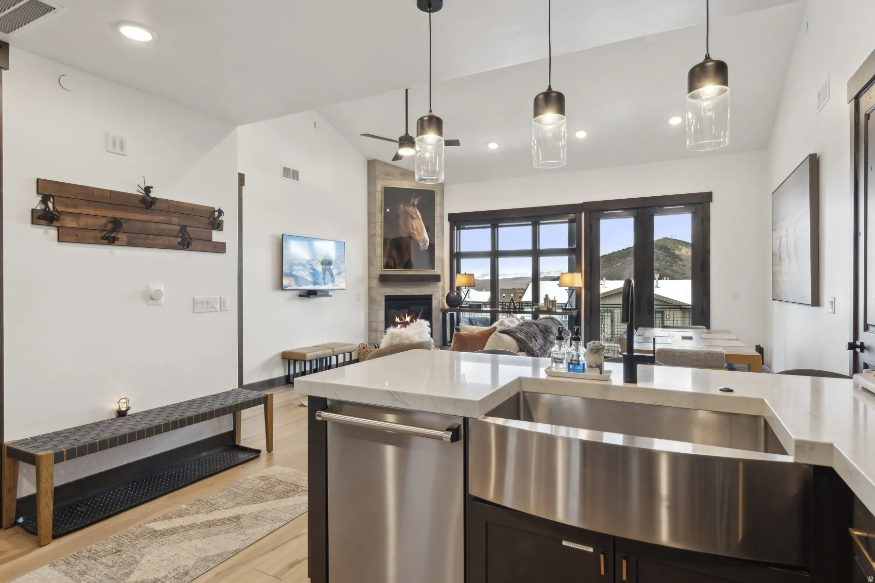 Kitchen with vaulted ceiling, light stone counters, light wood finished floors, stainless steel dishwasher, and a tile fireplace