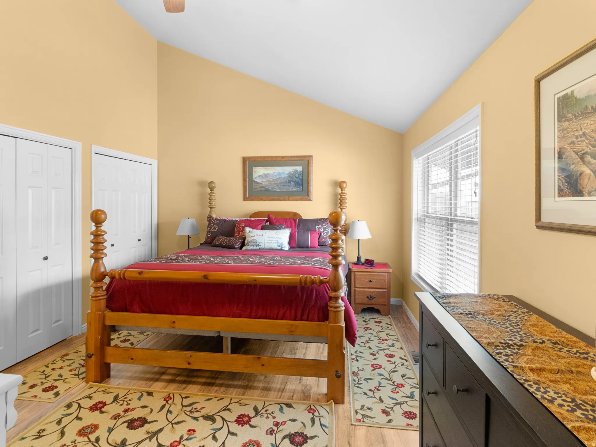 Bedroom with two closets, light wood-style flooring, a ceiling fan, and high vaulted ceiling
