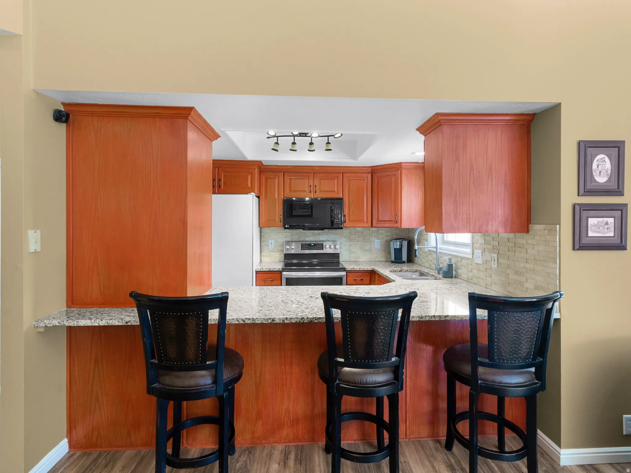 Kitchen with stainless steel electric range oven, light stone counters, backsplash, freestanding refrigerator, and black microwave