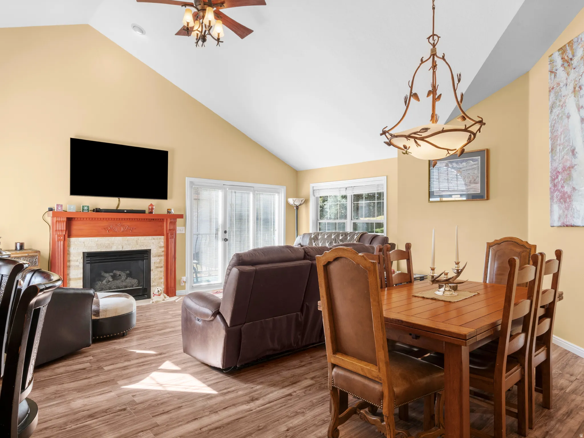 Dining space with light wood-style flooring, a high end fireplace, high vaulted ceiling, and a ceiling fan