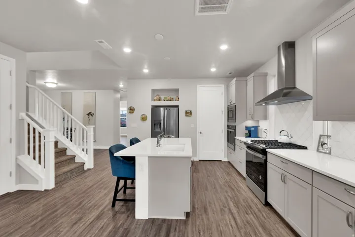 Kitchen featuring appliances with stainless steel finishes, wall chimney exhaust hood, a kitchen bar, gray cabinetry, and a center island with sink