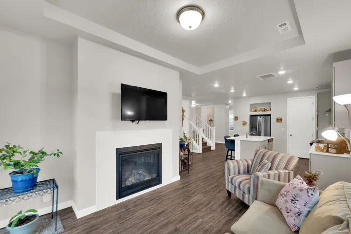 Living room featuring a glass covered fireplace, recessed lighting, stairway, dark wood-type flooring, and a raised ceiling