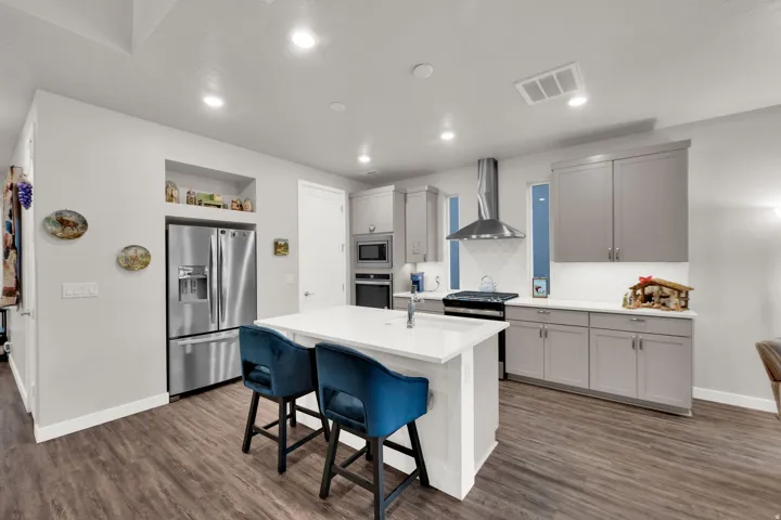 Kitchen featuring wall chimney range hood, a breakfast bar area, gray cabinets, appliances with stainless steel finishes, and an island with sink