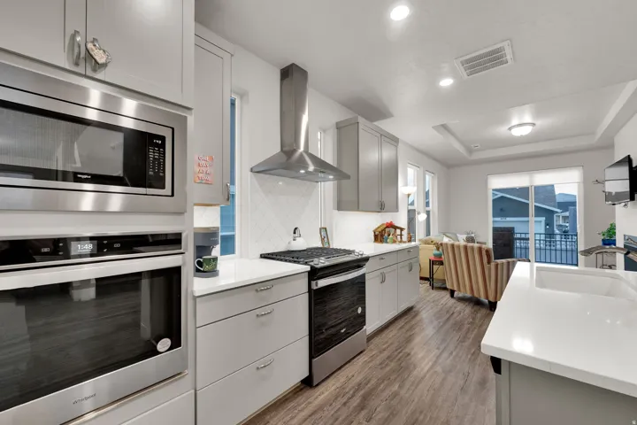 Kitchen with appliances with stainless steel finishes, gray cabinets, wall chimney exhaust hood, dark wood-type flooring, and recessed lighting
