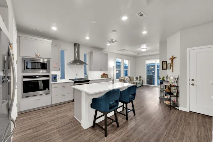 Kitchen with a kitchen breakfast bar, appliances with stainless steel finishes, wall chimney range hood, an island with sink, and decorative backsplash