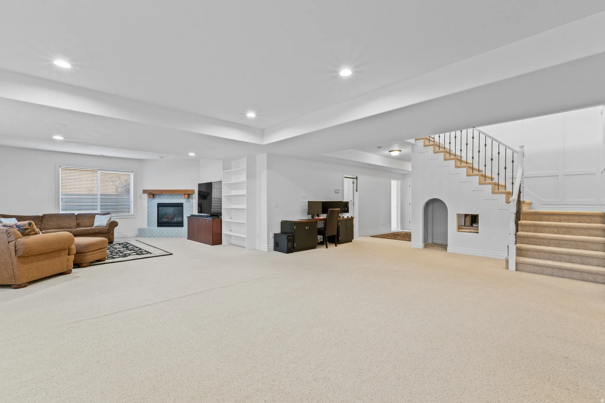 Living room featuring an office area, light colored carpet, a glass covered fireplace, recessed lighting, and stairs