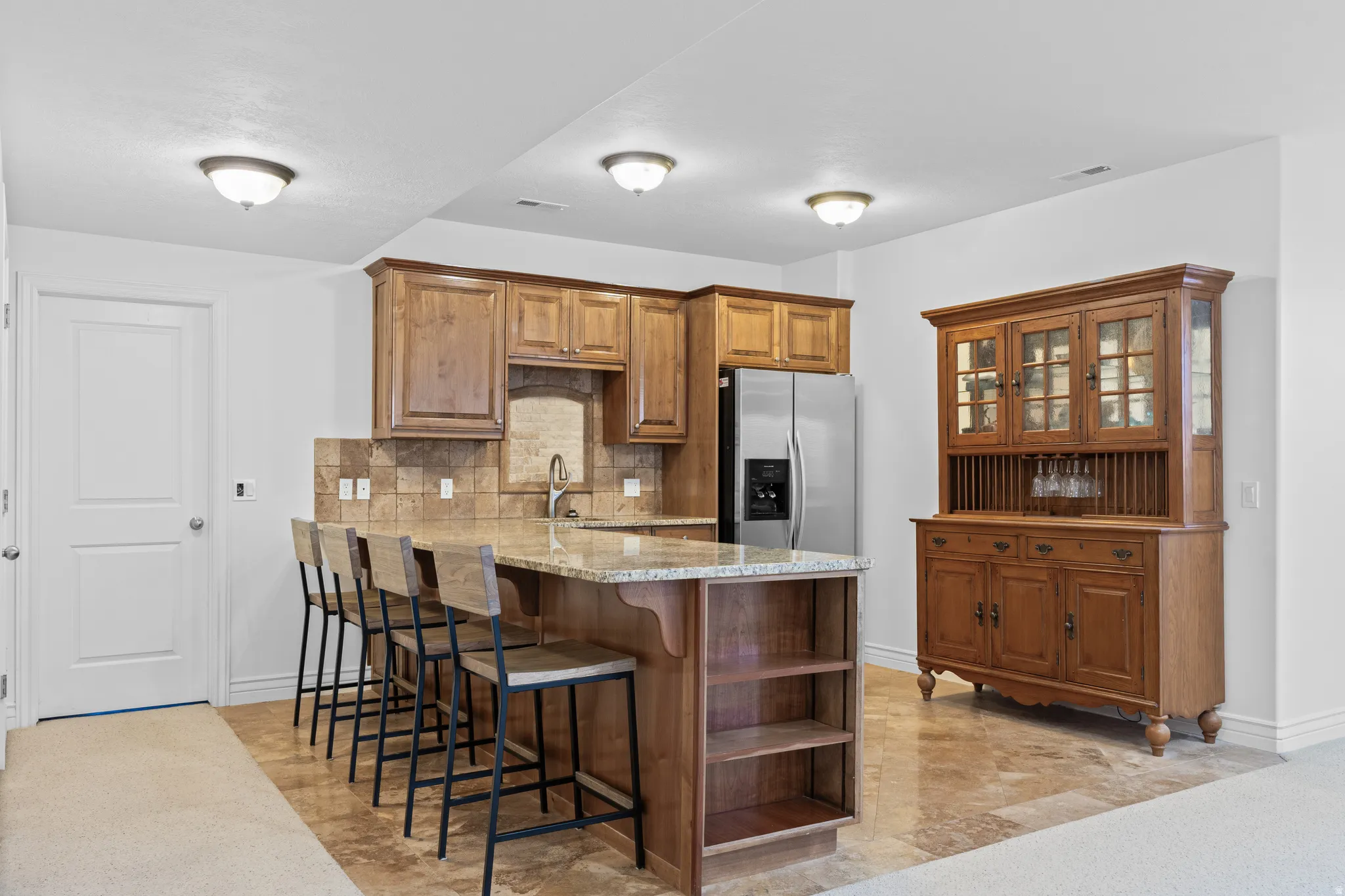 Kitchen featuring a breakfast bar area, brown cabinets, a peninsula, light stone counters, and tasteful backsplash