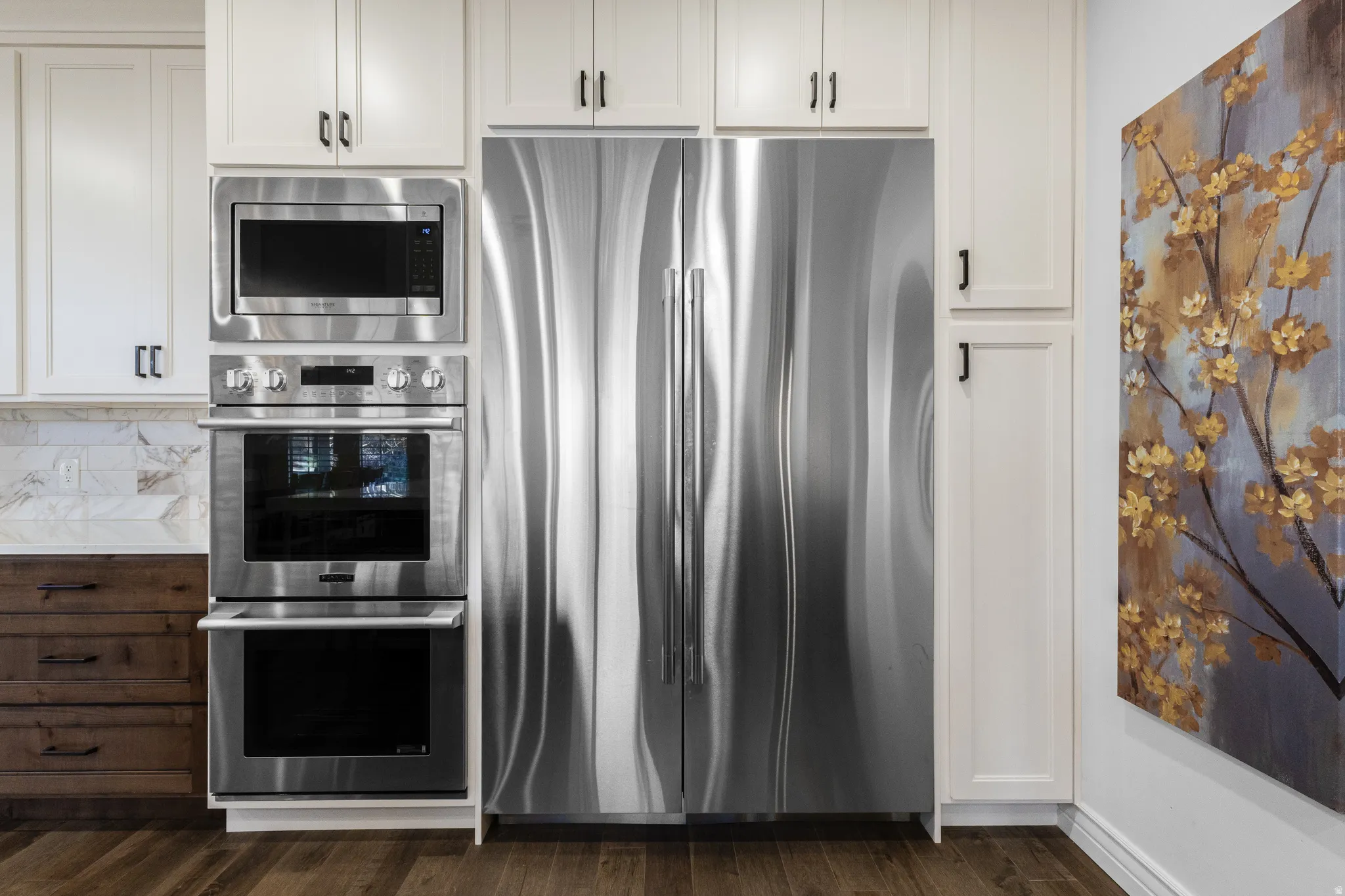 Kitchen featuring stainless steel appliances, white cabinets, backsplash, light countertops, and dark wood finished floors