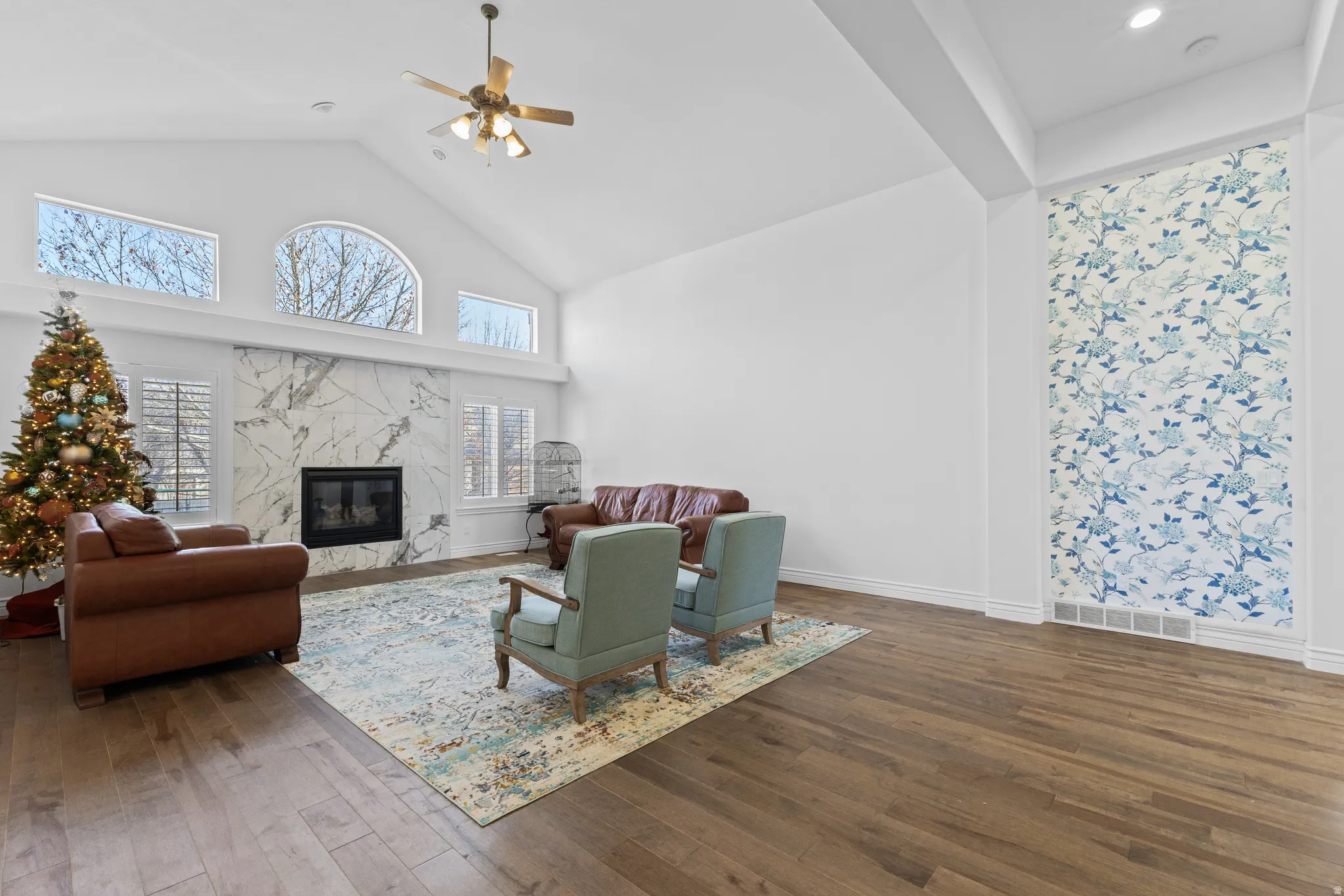 Living room with high vaulted ceiling, a premium fireplace, dark wood-style flooring, ceiling fan, and plenty of natural light