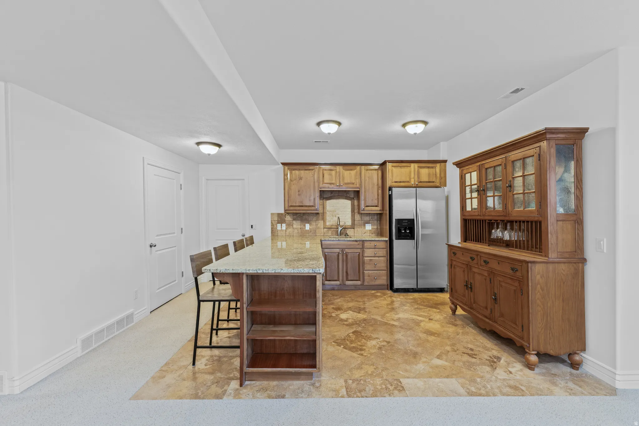 Kitchen featuring a peninsula, a breakfast bar, stainless steel refrigerator with ice dispenser, brown cabinets, and tasteful backsplash