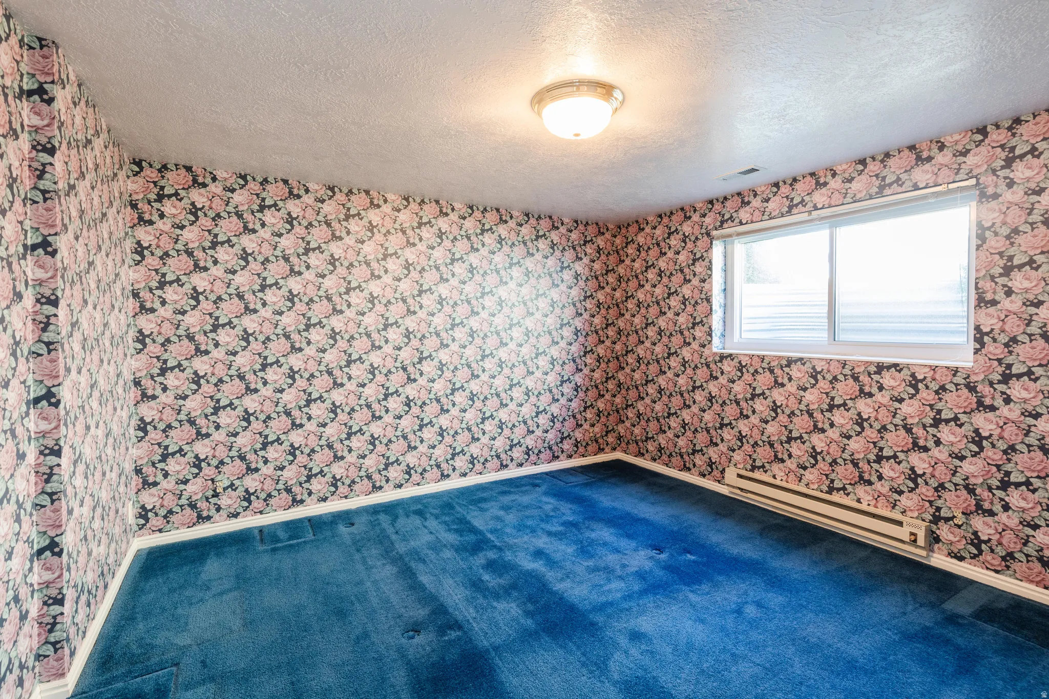 Carpeted empty room featuring a textured ceiling, a baseboard radiator, and wallpapered walls