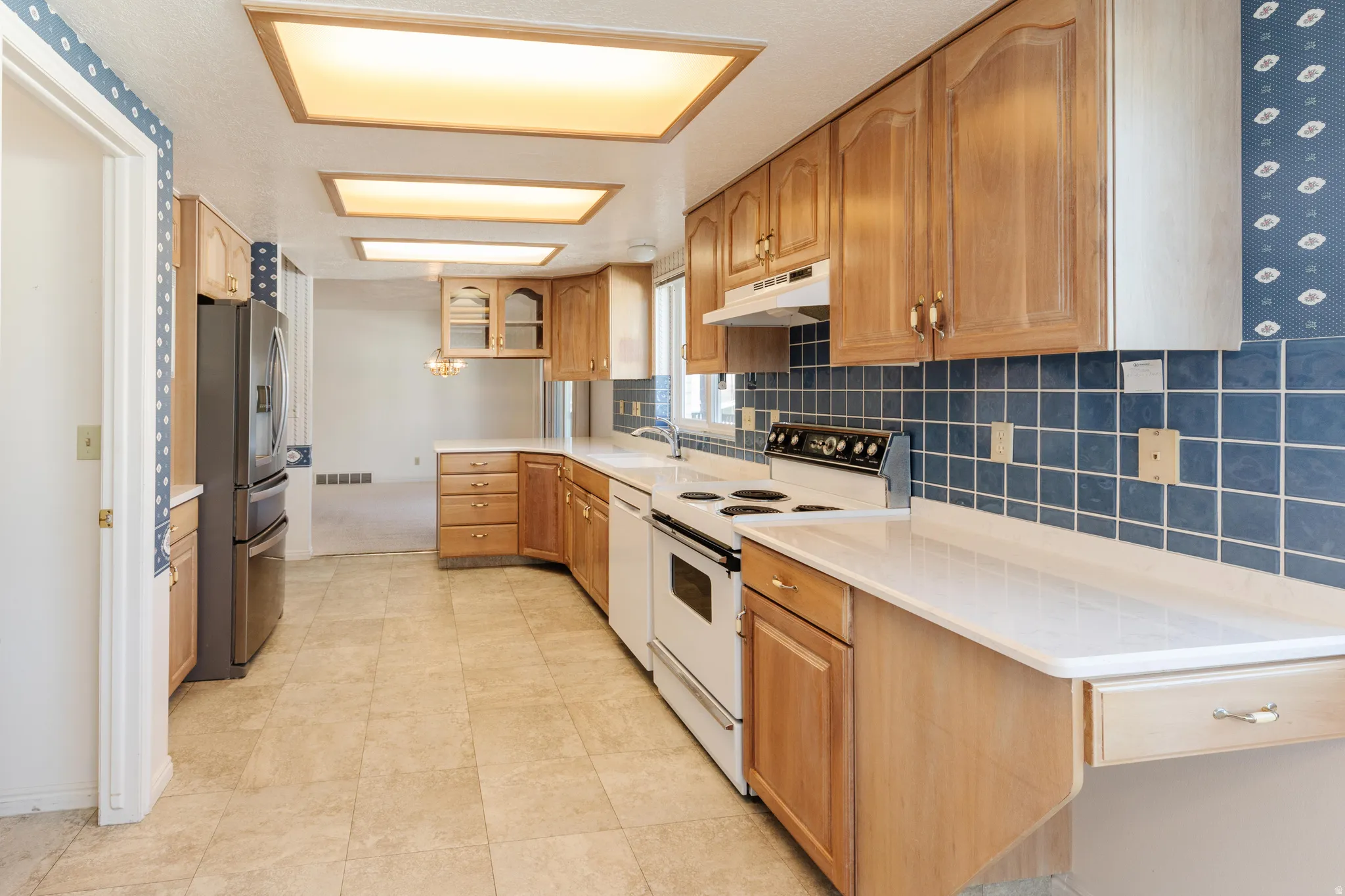 Kitchen featuring white appliances, backsplash, glass insert cabinets, under cabinet range hood, and brown cabinetry