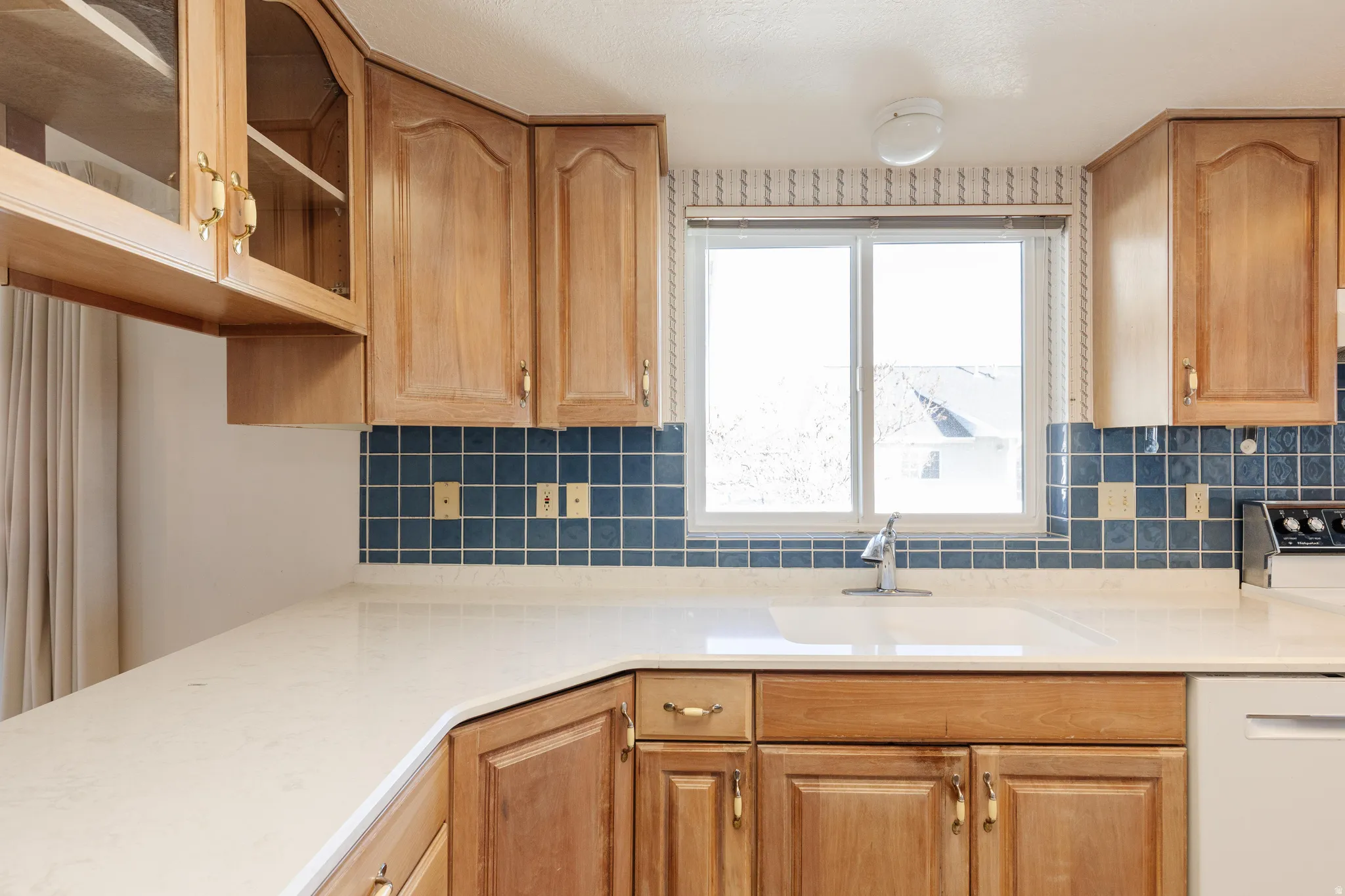 Kitchen with glass insert cabinets, white appliances, tasteful backsplash, and light stone counters