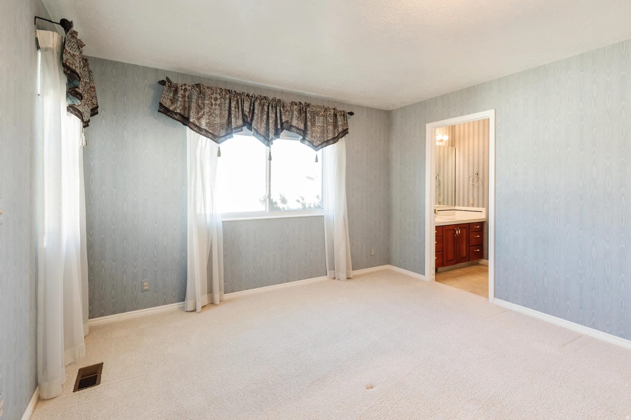 Unfurnished bedroom with light carpet, ensuite bath, and wallpapered walls