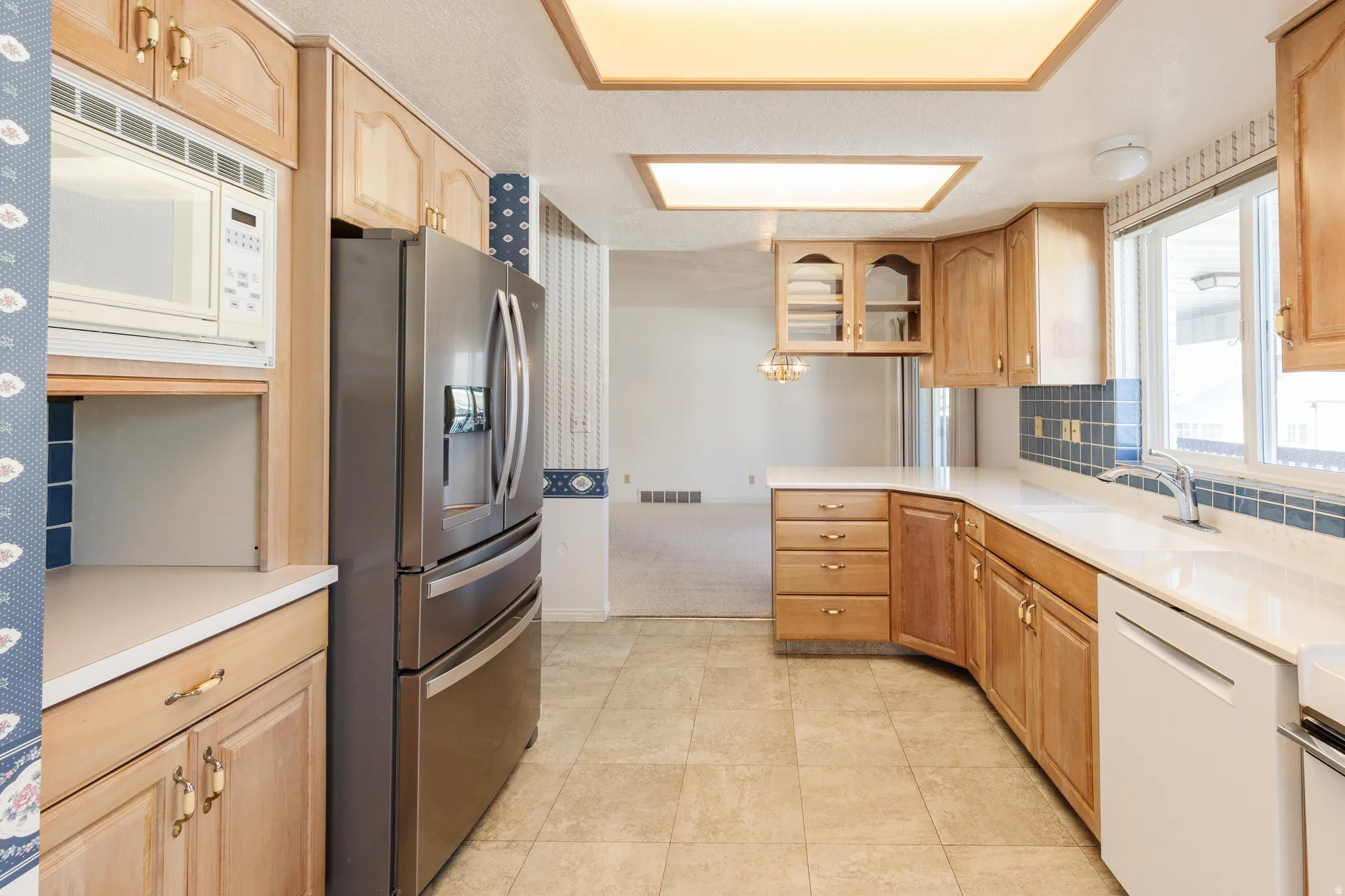 Kitchen with white appliances, light countertops, glass insert cabinets, and tasteful backsplash