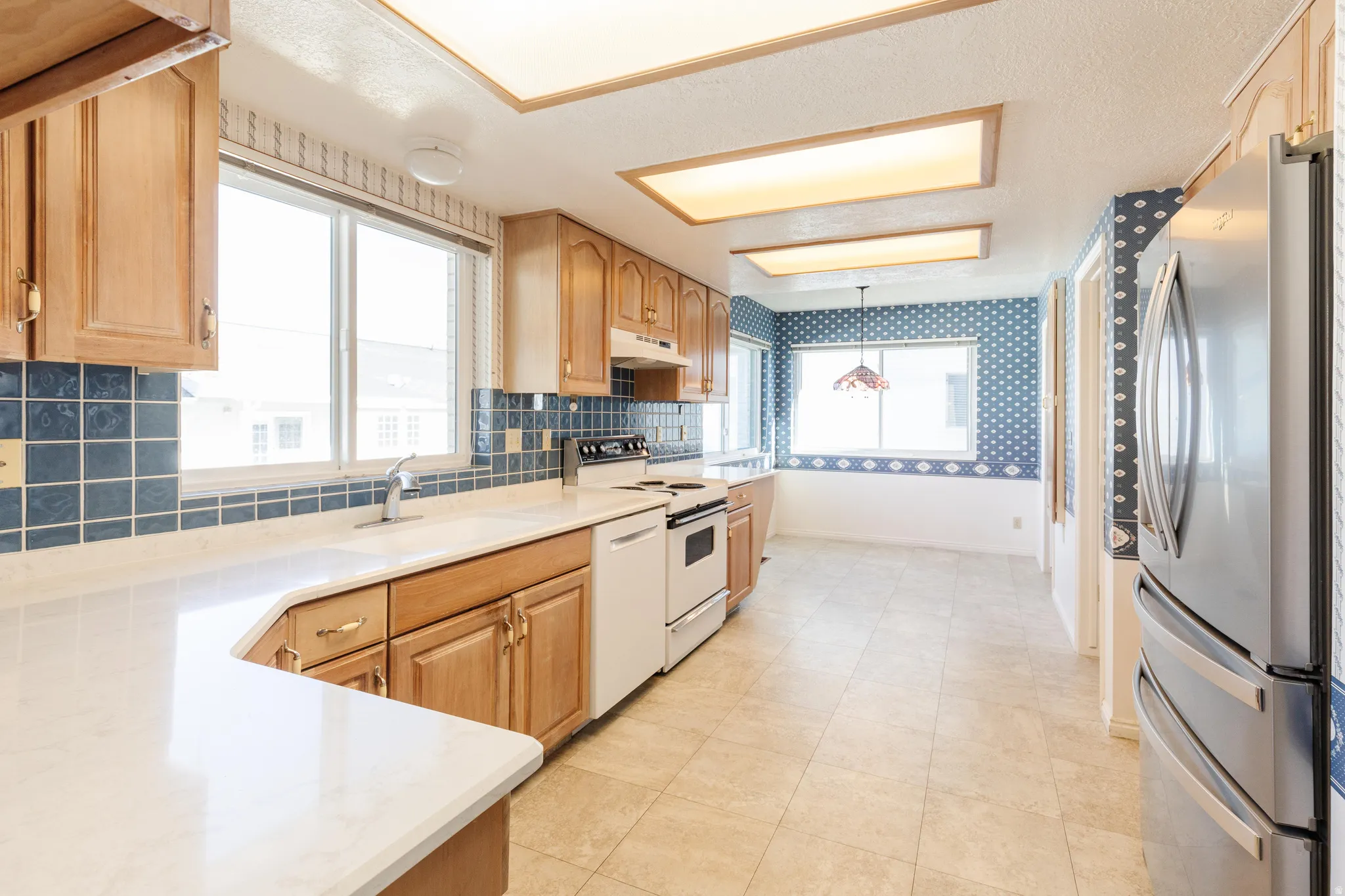 Kitchen featuring white appliances, healthy amount of natural light, decorative backsplash, wallpapered walls, and light stone counters