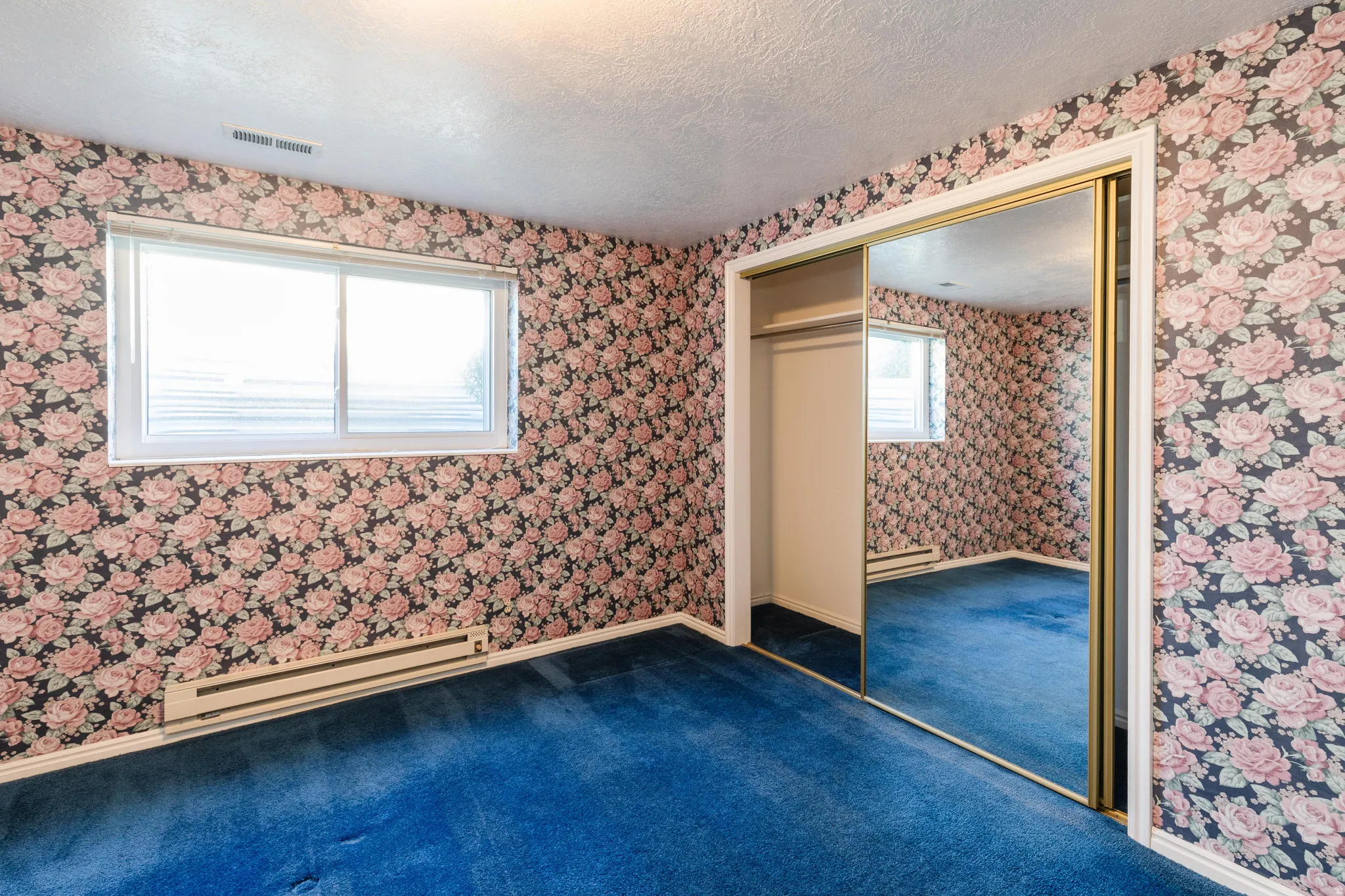 Unfurnished bedroom with a baseboard radiator, a textured ceiling, dark carpet, wallpapered walls, and a closet