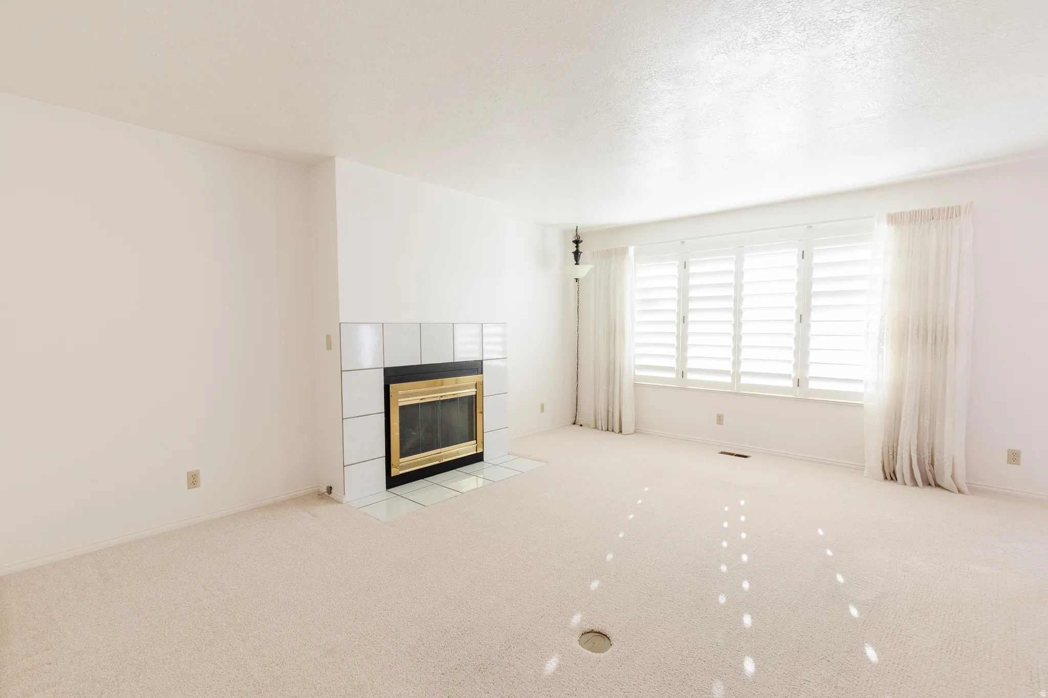 Unfurnished living room featuring a fireplace, light carpet, and a textured ceiling