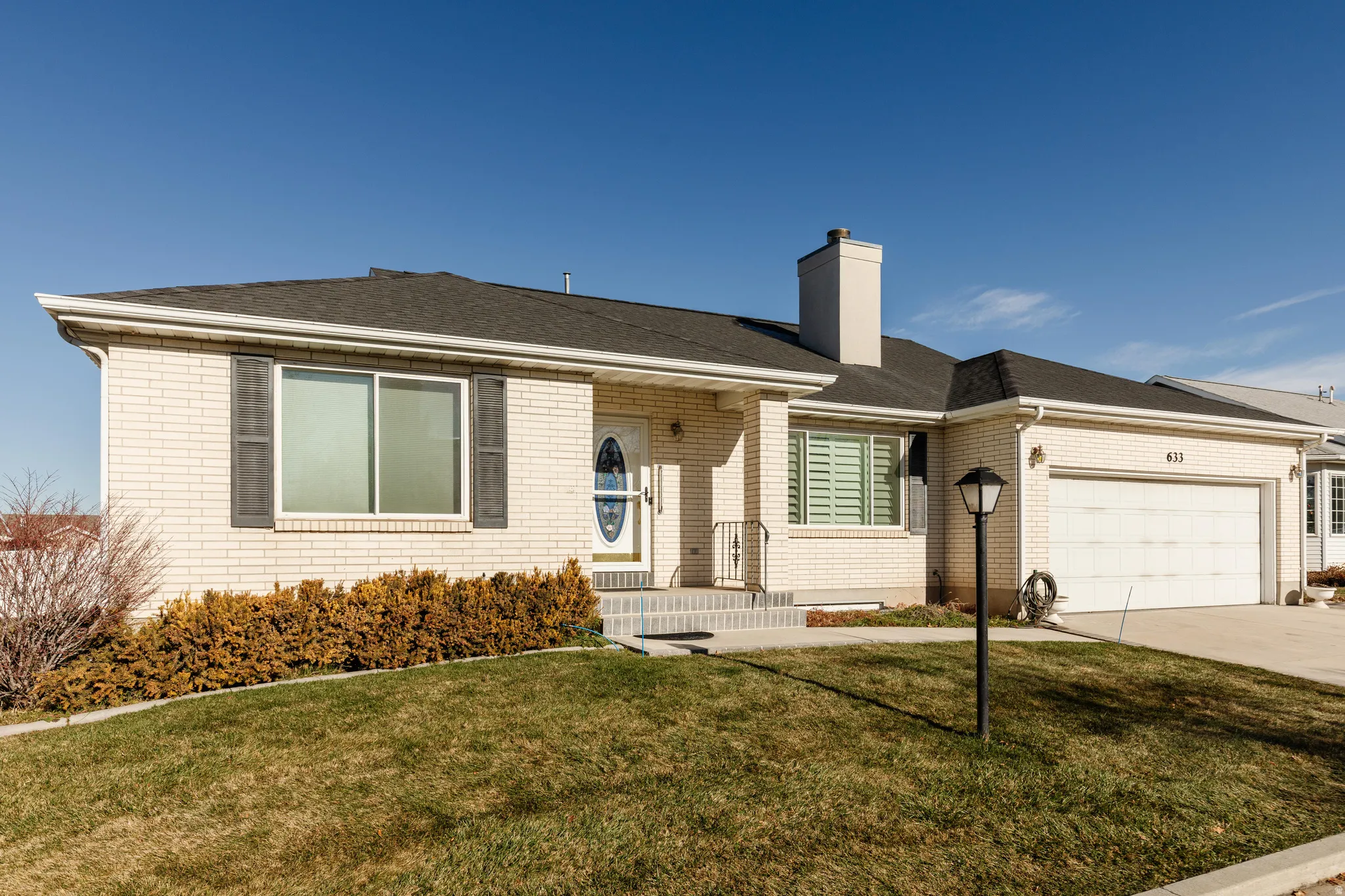 Ranch-style home featuring a front lawn, a chimney, driveway, and brick siding