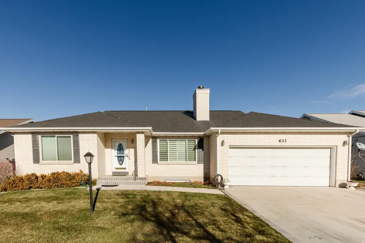Single story home featuring brick siding, a chimney, driveway, a front lawn, and an attached garage