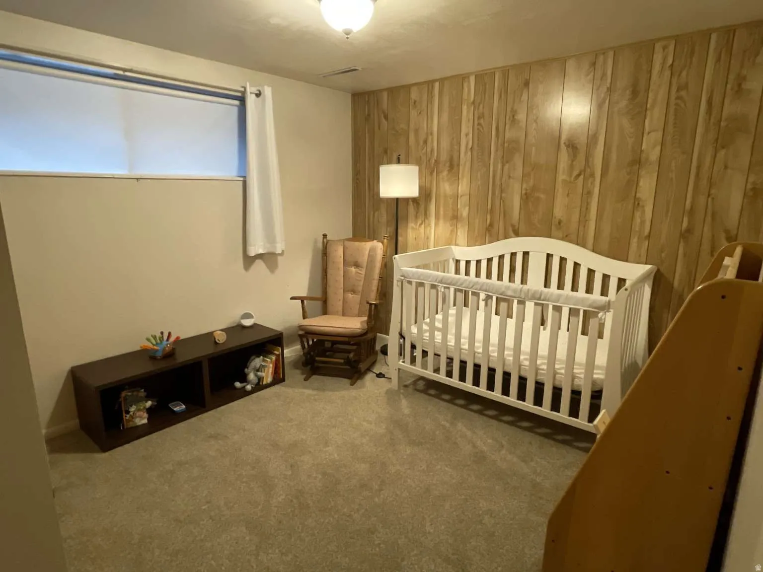 Bedroom featuring wood walls, a crib, and carpet flooring