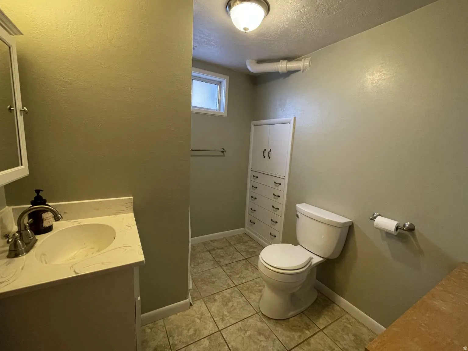 Bathroom with a textured ceiling, vanity, light tile patterned floors, and a textured wall